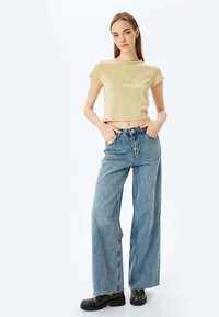 Afskåret, lysegrøn t-shirt med stjernesyning, parret med løse, højtaljede blå jeans og sorte platformstøvler.