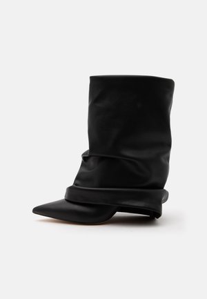 Schwarzer lässiger Lederstiefel bis zur Mitte der Wade mit spitzer Zehe und niedrigem Absatz vor weißem Hintergrund.