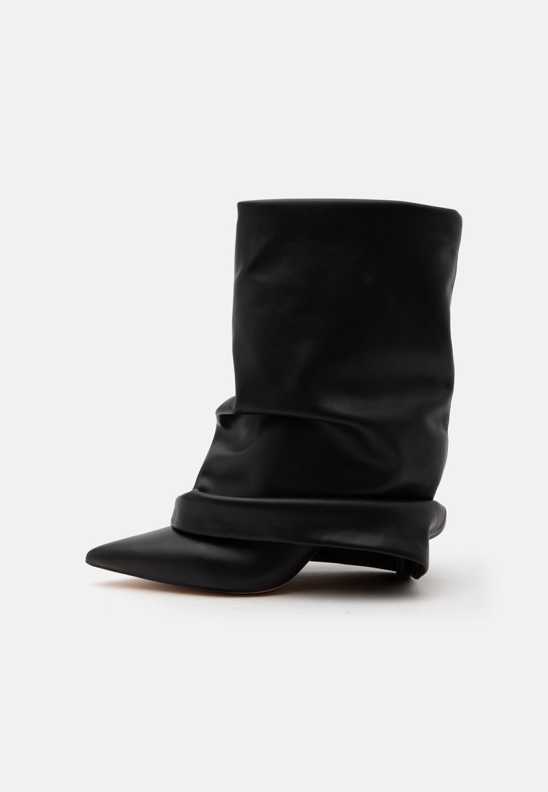 Botte en cuir noire ample mi-mollet avec bout pointu et petit talon sur fond blanc.