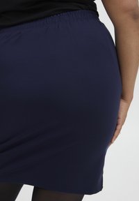 Jupe élastique bleu marine avec une texture lisse, arrivant à mi-cuisse. Design simple sans motifs visibles ni détails matériels.