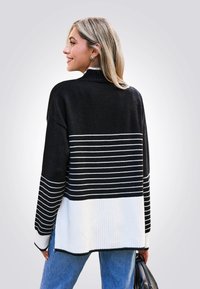 Schwarz-weißt gestreifter Pullover mit hohem Kragen und geripptem Saum, der eine lockere Passform und eine weiche Textur bietet. Lässiger Look, kombiniert mit Jeans.