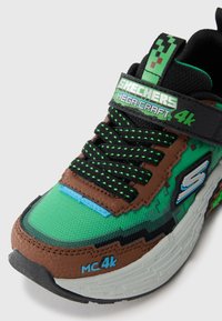 Groene en bruine Skechers Mega-Craft 4K sneaker met pixelachtig ontwerp, zwarte en groene veters, en de tekst "MC 4k" op de witte zool.