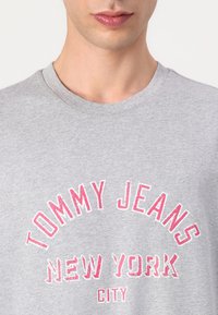 Grå bomulls t-skjorte med "TOMMY JEANS NEW YORK CITY" i fet, slitt rosa skrift. K klassisk rund hals og korte ermer.