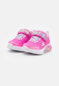 Różowe buty sportowe z siateczkową cholewką, kontrastującymi fioletowymi akcentami, dekoracyjnymi wzorami zwierząt na pasku oraz wyściełaną białą podeszwą.