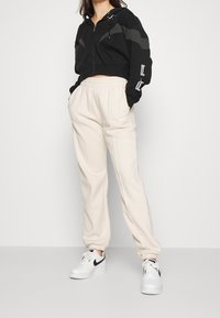 Black cropped hoodie with gray accents, paired with cream joggers featuring elastic cuffs and a Nike logo. White sneakers complete the outfit.