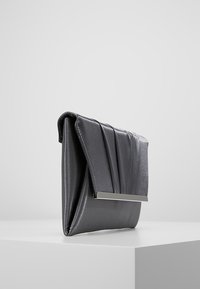Pochette en cuir synthétique gris avec un design plissé, accent métallique à l'avant et texture lisse. Forme rectangulaire compacte.