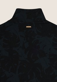 Pullover nero con colletto alto, caratterizzato da un motivo a foglia tono su tono. Include un'etichetta del marchio in metallo dorato sul retro. Tessuto morbido.