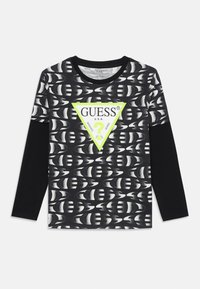 Svart langermet skjorte med grafisk mønster og en neon grønn trekantlogo i midten med "GUESS"-tekst, laget av myk stoff.