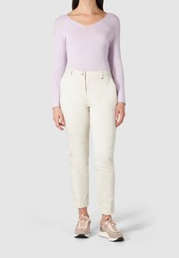 Haut à manches longues couleur lavande claire avec un col en V, associé à un pantalon ajusté blanc cassé et des baskets beige avec des accents rose pâle.