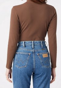 Top de manga larga marrón con canalé, combinado con jeans de mezclilla azul de tiro alto, que presentan bolsillos traseros con acentos de costura y una etiqueta de la marca.