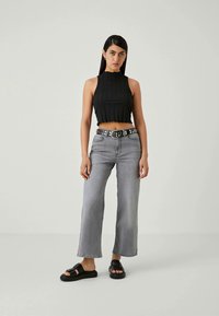 Zwarte geribbelde crop top, grijze wijde spijkerbroek met een gesp met studs, en zwarte slider sandalen. Eenvoudig ontwerp met gladde texturen.