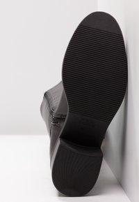 Czarna podeszwa botków za kostkę z żebrowanym i wzorzystym bieżnikiem, blokowy obcas, zamek błyskawiczny z boku oraz oznaczenia rozmiaru na białym tle.