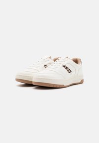 Bílé kožené tenisky s texturovaným designem, kulatou špičkou, kontrastní hnědou gumovou podrážkou a akcentem v leopardím vzoru na bocích.