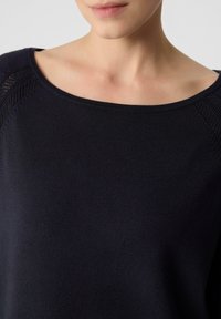 Granatowy dzianinowy top z szerokim dekoltem, z teksturowanym wykończeniem wzdłuż szwów na ramionach. Gładki, miękki materiał.