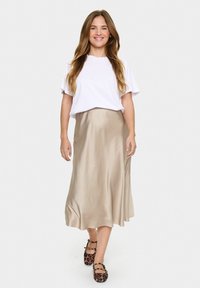 Satiini beige midi-hame, jossa on sileä pinta, yhdistettynä valkoiseen t-paitaan. Käytetään mustien kengillä, joissa on leopardikuosiset yksityiskohdat.