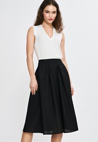 Czarna plisowana spódnica midi z wysokim stanem, zestawiona z białym bezrękawnikiem z dekoltem w serek. Gładki materiał, prosty krój, minimalne akcenty.