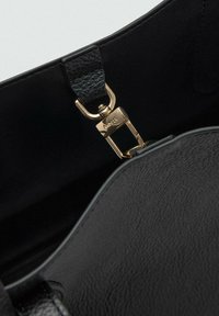 Interno di una borsa a tracolla in pelle nera con una tracolla testurizzata e una chiusura in metallo dorato incisa, evidenziando la funzionalità e i dettagli di design.