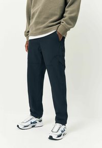 Ciemnoniebieskie spodnie slim fit z bocznymi kieszeniami i subtelnymi detalami przeszycia, w połączeniu z białymi i szarymi butami sportowymi.
