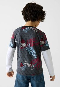 Szary t-shirt z grafiką w stylu graffiti w kolorach czerwonym, niebieskim i białym; długie białe rękawy; wykonany z bawełny; luźny krój.