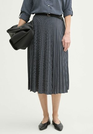 Jupe plissée noir et bleu avec un motif géométrique, associée à une ceinture noire ajustée et un sac à bandoulière noir. Portée avec des chaussures plates noires.