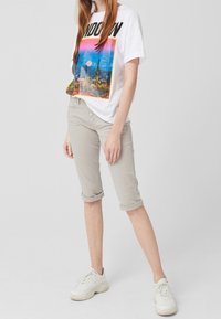 Camiseta gráfica blanca con el texto "LONDRES", que presenta una impresión colorida del horizonte de la ciudad. Pantalones ligeros grises enrollados y zapatillas blancas.