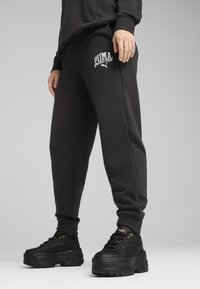 Zwarte sweatpants met een losse pasvorm, voorzien van een wit Puma-logo op de dij. Het materiaal lijkt zacht; inclusief elastische boorden en zakken.