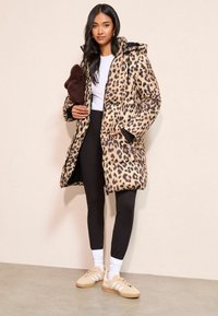 Leopardimustriga pintsakjope kapuutsiga, tõmblukuga, mustade detailidega, kantud valge topi ja mustade retuuside peal, beežide tossudega.