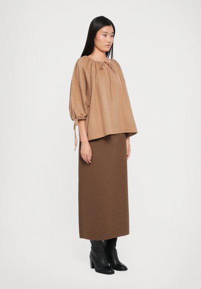 Brauner Wollpullover mit Puffärmeln und gerafftem Halsband. Enganliegender brauner Wollrock, kombiniert mit schwarzen, hohen Stiefeletten.