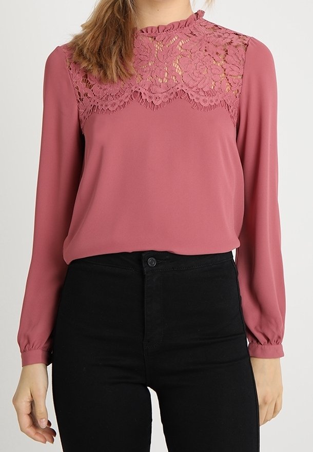 Blus med långa ärmar i dammros med spetsdetaljer vid axelpartiet. Slät i tyget, åtsittande midja och elastiska ärmslut. Matchas med svarta byxor.