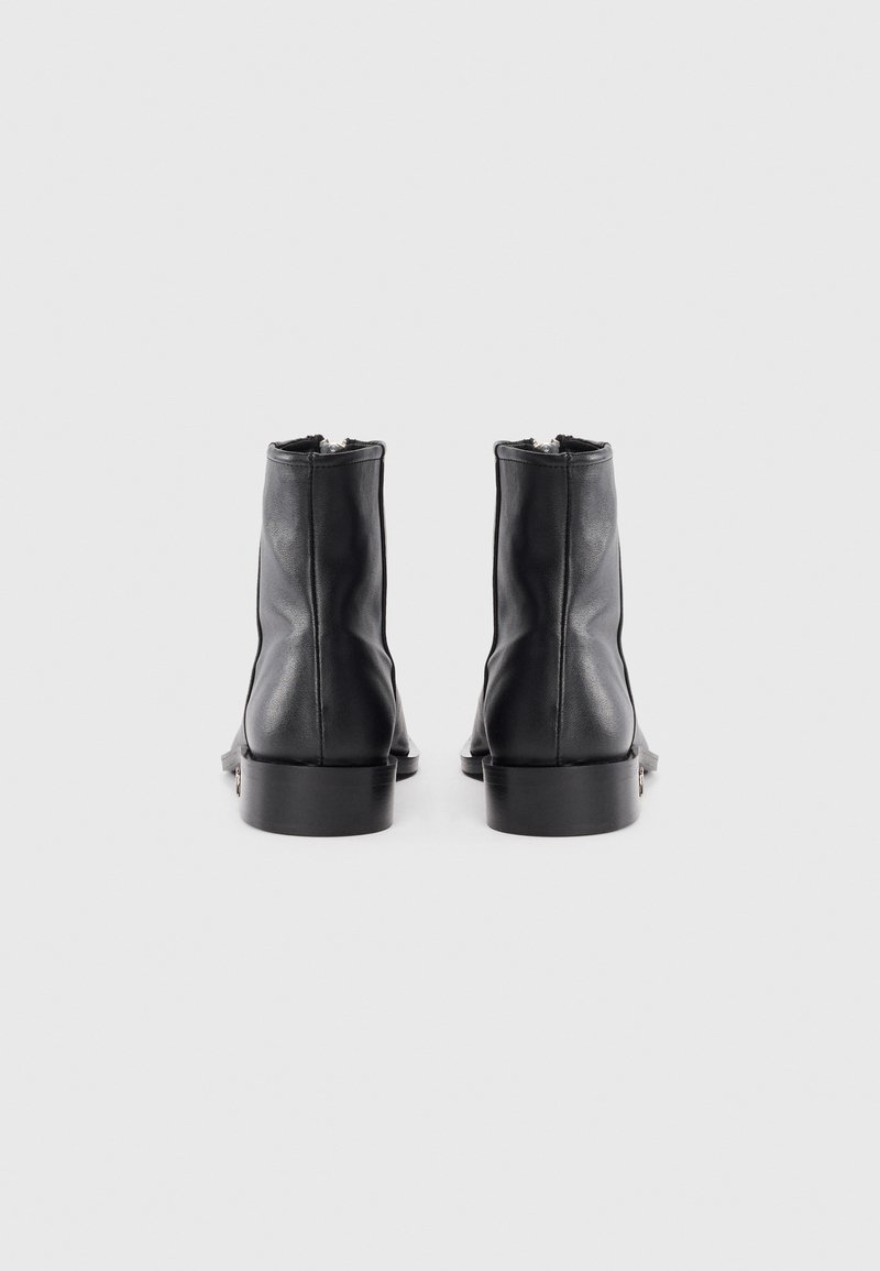 Bottes de cheville en cuir noir avec une texture lisse, dotées d'un petit talon épais et d'un design minimaliste. Fermetures éclair à l'arrière pour un enfilage facile.