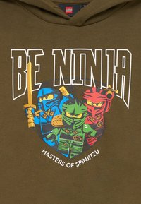 Olivinė džemperis su grafiniu atspaudu, vaizduojančiu tris ninjas mėlyna, žalia ir raudona spalvomis, su užrašais "BŪK NINJA" ir "MASTERS OF SPINJITZU."
