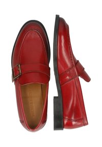 Mocassini in pelle rossa con dettaglio a strappo e fibbia, punta arrotondata e tacco basso nero. Texture liscia e finitura lucida.