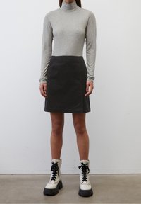Graues Longsleeve-Turtleneck-Oberteil und einen schwarzen Rock, kombiniert mit weißen Schnürstiefeletten mit schwarzen Sohlen. Einfaches Design, glatte Textur.