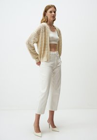 Słomkowy kardigan z koronkowym splotem, z opadającymi ramionami, noszony na dopasowanej białej bluzce crop top oraz na wysokim stanie białych spodniach. Eleganckie szpilki o spiczastym nosku.