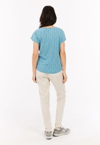 Šviesiai mėlyna raštuota marškinėliai su trumpomis rankovėmis, derinami su smėlio spalvos kelnėmis ir pilkais sportbačiais. Marškiniai turi tekstūrinį, geometrinį raštą.