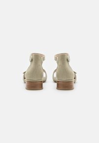 Beige Wildleder-Absatzsandalen mit einem zweifarbigen Holzblockabsatz. Sie verfügen über einen offenen Rücken und einen Knöchelriemen mit aufwendigen Webdetails.