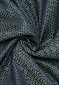 Dunkelblauer Stoff mit metallischem goldenen Diamantmuster, leicht zerknittert und in der Mitte gefaltet.