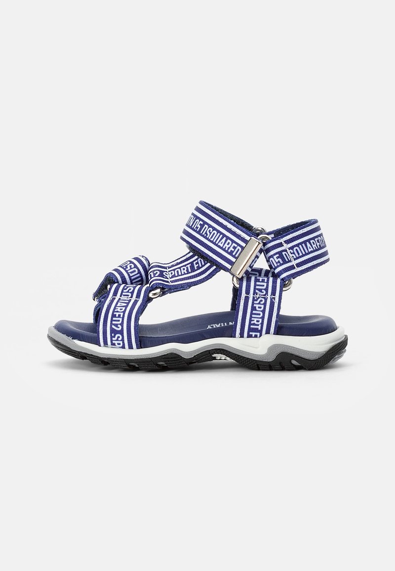 Sandales sportives bleues et blanches avec des sangles ajustables, semelle en caoutchouc texturée et détails de marque sur les sangles. Conçues pour le confort et la flexibilité.