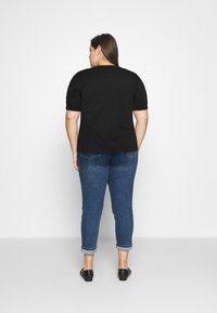 Černý top s krátkým rukávem a hladkou texturou, spárovaný s modrými džíny s ohrnutými manžetami. Tento outfit má ležérní design vhodný pro každodenní nošení.