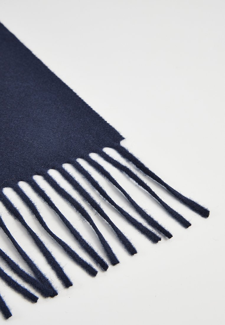 Sciarpa in lana blu navy con bordi frangiati, caratterizzata da una consistenza morbida e una finitura liscia. La lunghezza include molte frange lunghe e affusolate.