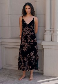 Abito nero a fiori con scollo a V e spalline sottili. Presenta motivi floreali color oro rosa su un tessuto liscio e fluente, che arriva fino a metà polpaccio.