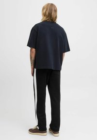 Marineblå bomulds t-shirt med en afslappet pasform, parret med sorte sweatpants med hvide sidelister og brune sneakers.