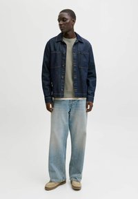 Tumši zila džinsu jaka ar divām krūšu kabatām, valkāta pār gaiši zaļu sporta krekliņu. Gaiši zilas plaša piegriezuma džinsa bikses un bēšas kurpes.