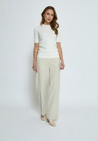 Vit kortärmad stickad topp i kombination med beige vida byxor och hudfärgade spetsskor, vilket skapar en ljus, neutral outfit.