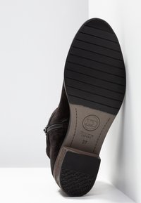 Semelle noire d'une botte en daim marron avec une fermeture éclair sur le côté, montrant le motif de la bande de roulement et le logo Dunne London en taille 37.