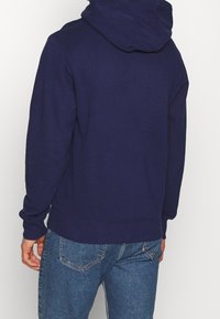 Navy modrá bavlněná mikina s velkou kapucí a ribbovanými manžetami; má plochý lem a uvolněný střih; minimalistický design, žádné viditelné grafiky.