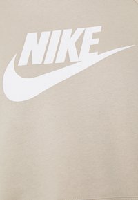 Felpa beige in tessuto morbido con grande logo bianco "NIKE" e design swoosh stampati sul davanti.