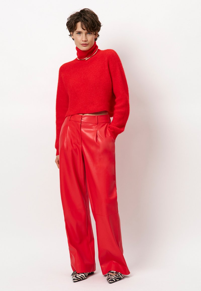 Rode cropped trui met hoge kraag, gecombineerd met hoge taille, rode faux leren wijde broek en zwart-witte gestreepte puntige schoenen.
