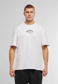 White cotton t-shirt with short sleeves featuring a black graphic print of “KANI” and “Brooklyn NYC” on the chest. Simple design, crew neckline.