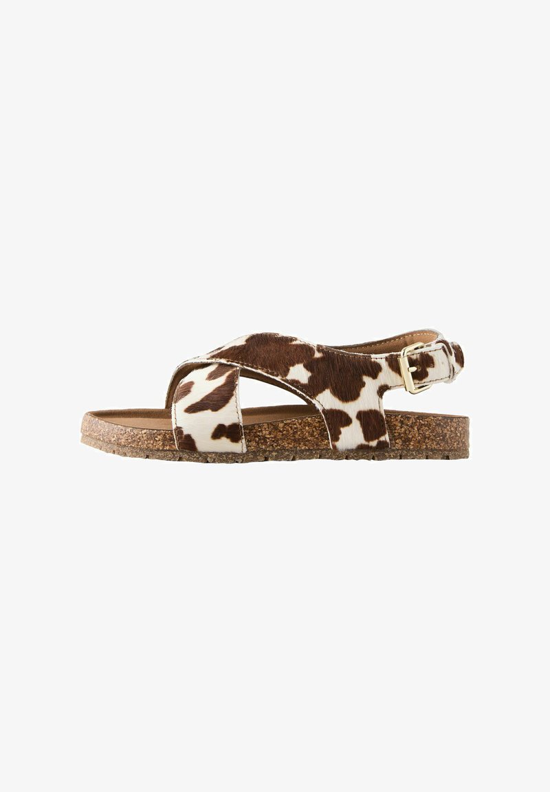 Sandale à motif peau de vache marron et blanc avec des sangles croisées, une boucle dorée et une semelle en liège.